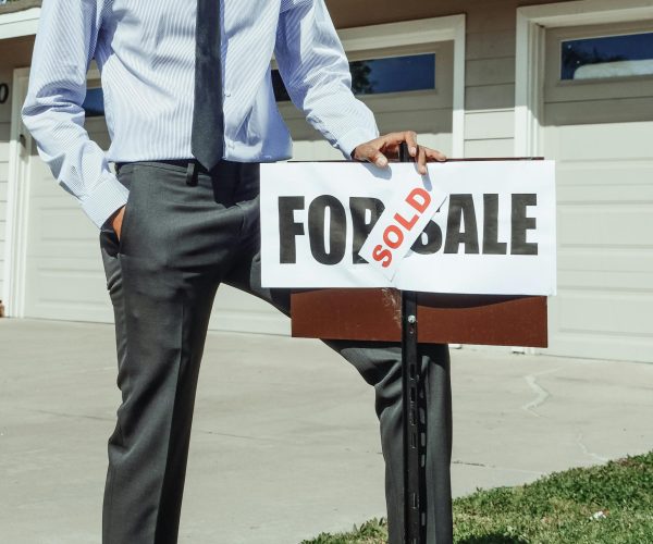 Man in Blue Dress Shirt Holding a Sold Sign